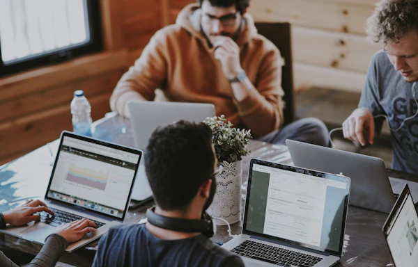 Four people working on laptops around a table with a potted plant in the middle