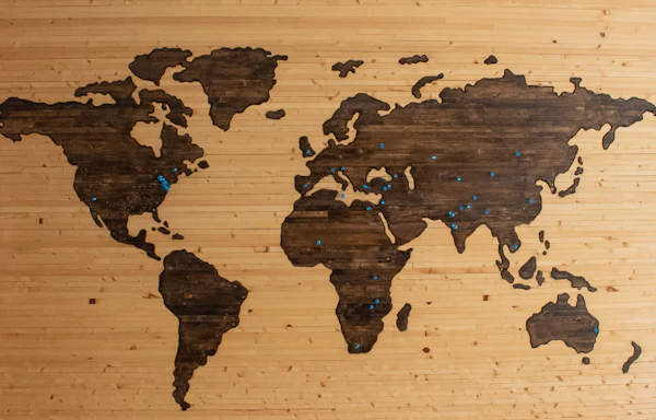Dark wooden world map set into a light wood wall, marked with blue pins