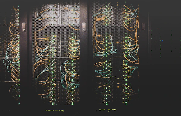 Server racks full of orange and blue cables with green status lights in the dark