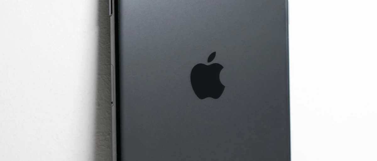 Beyaz duvara dayalı koyu gri akıllı telefonun Apple logolu arka yüzünün yakın çekimi