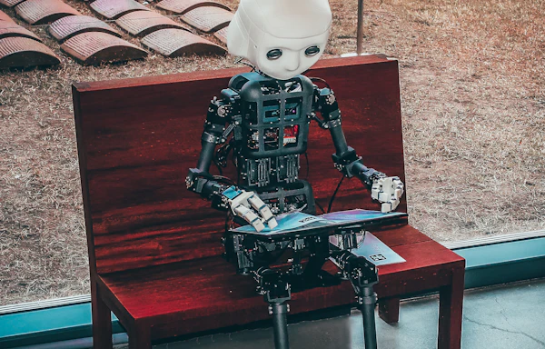 Kırmızı ahşap bir bankta oturup kucağındaki açık kitapçığa dokunan insansı robot